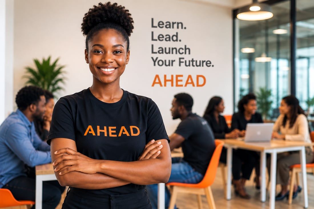 An AHEAD learner in an AHEAD T-shirt standing in a shared workspace, with colleagues working at desks behind and a wall reading “Learn. Lead. Launch Your Future. AHEAD”.